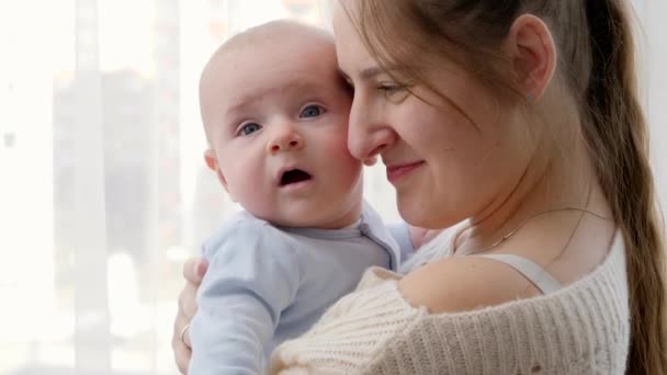 Evdeki büyük pencerede sarılıp kucaklaşan anne ve bebeğin yakın plan portresi. Aile mutluluğu ve çocuk gelişimi kavramı - Video, Çekim