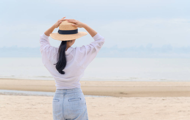 Открытый летний портрет молодой женщины в соломенной шляпе, смотрящей на море на пляже, наслаждающейся свободой, свежим воздухом и незабываемым отпуском - Фото, изображение