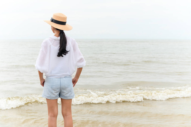 熱帯のビーチで海を探しているわら帽子の若いアジアの女性の屋外夏の肖像画は、自由時間、新鮮な空気とレジャー旅行休暇をお楽しみください - 写真・画像