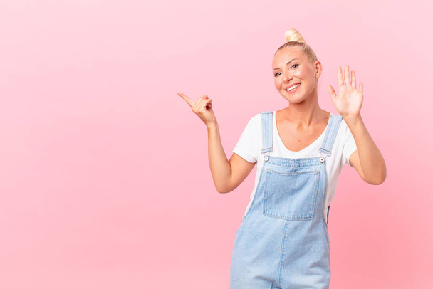 pretty blond woman smiling happily, waving hand, welcoming and greeting you - Фото, изображение