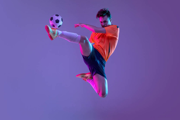 Young caucasian man, male soccer football player training isolated on gradient blue pink background in neon light - Photo, Image