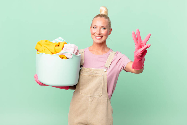 pretty blond woman smiling and looking friendly, showing number three washing clothes concept - Foto, immagini