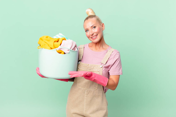 pretty blond woman smiling cheerfully, feeling happy and showing a concept washing clothes concept - 写真・画像