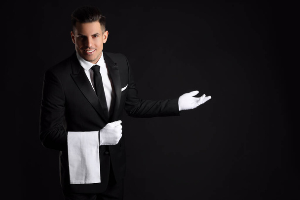 Handsome butler with towel on black background, space for text - Foto, afbeelding