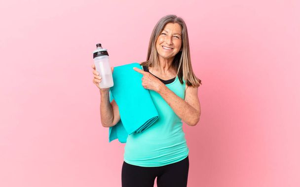 pretty middle age woman smiling cheerfully, feeling happy and pointing to the side. fitness concept - Photo, Image