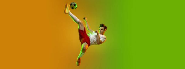 Young caucasian man, male soccer football player training isolated on gradient yellow green background in neon light - Foto, Imagen
