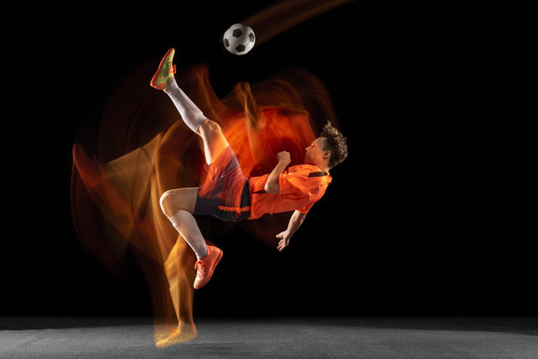 Young caucasian male football or soccer player kicking ball for the goal in mixed light on dark background. Concept of healthy lifestyle, professional sport, hobby. - 写真・画像
