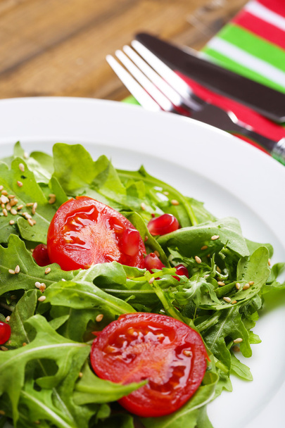 Green salad made with  arugula, tomatoes and sesame  on plate, on wooden background - Foto, Imagem