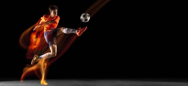 Young caucasian male football or soccer player kicking ball for the goal in mixed light on dark background. Concept of healthy lifestyle, professional sport, hobby. - Fotografie, Obrázek