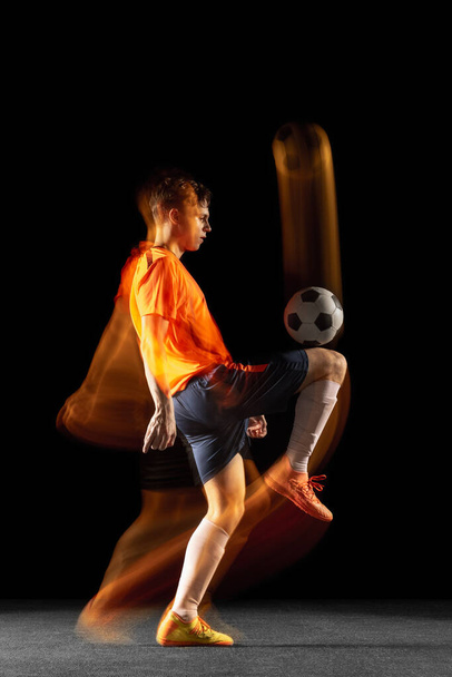 Young caucasian male football or soccer player kicking ball for the goal in mixed light on dark background. Concept of healthy lifestyle, professional sport, hobby. - Zdjęcie, obraz
