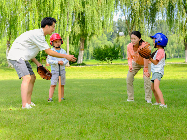 Happy family of four playing baseball in the park - Фото, изображение