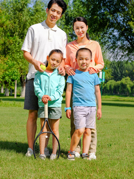 Happy family of four playing tennis in the park - Photo, Image