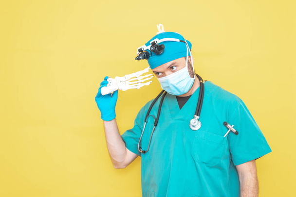 Sarı arka planda yeşil giyinmiş genç doktor-cerrah. - Fotoğraf, Görsel
