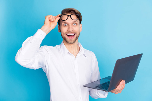 Photo of amazed happy shocked young man hold laptop wear glasses isolated on pastel blue color background - Fotoğraf, Görsel