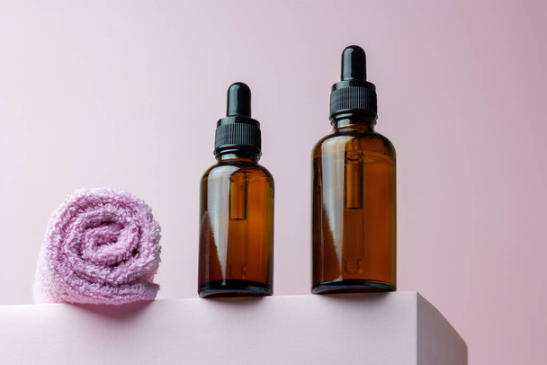 Trendy composition with dropper bottles with a face oil or serum and a towel on a pink podium. Natural organic cosmetic spa concept. Flat lay, copy space. - Fotó, kép
