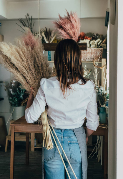 Précédent View of Unidentifiable Woman Holding Pampas in her Flower Shop.Rear view of female florist standing and working with pampas grass at her workshop studio. - Photo, image