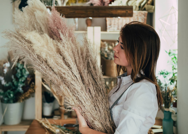 Молодая женщина-флорист с пампасами в руках стоит в цветочном магазине. - Фото, изображение