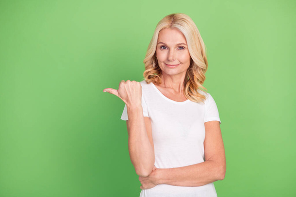 Photo of lovely blond elder lady point empty space wear white t-shirt isolated on green color background - Fotó, kép