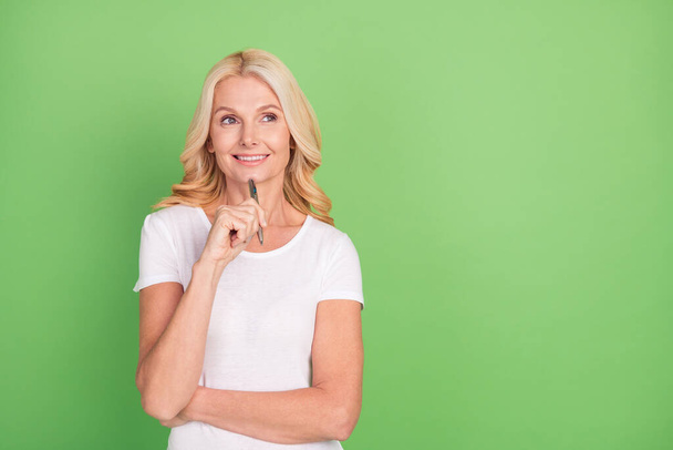 Photo of cute business blond aged lady hold pen look empty space wear white t-shirt isolated on green color background - Foto, immagini