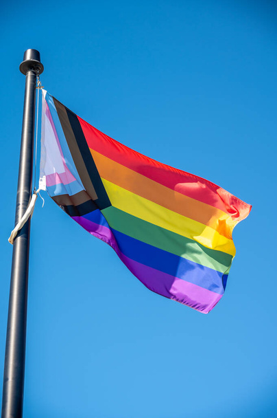 "Progress "Pride Flag against a blue sky - σημαία υπερηφάνειας και τα χρώματα της διαφανούς σημαίας υπερηφάνειας. - Φωτογραφία, εικόνα