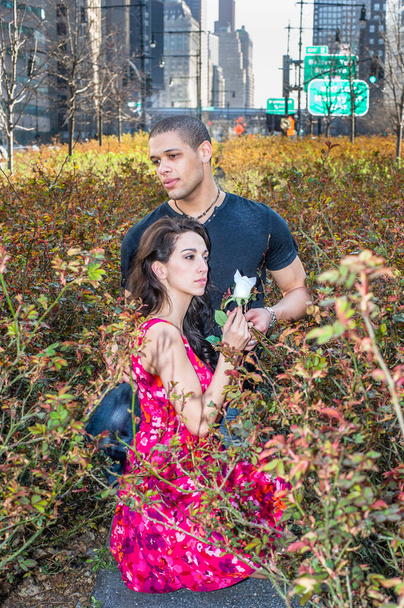 A young couple is passionately relying on each other in a rose garden in the center of the street, girl holding a white ros - Foto, imagen