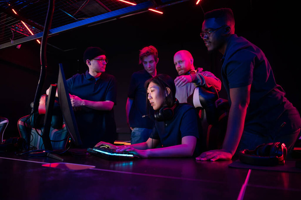 Ein Cyber-Team aus Jungs und einem Trainer erklärt einem neuen Teammitglied, einem asiatischen Mädchen, ihre Strategie - Foto, Bild