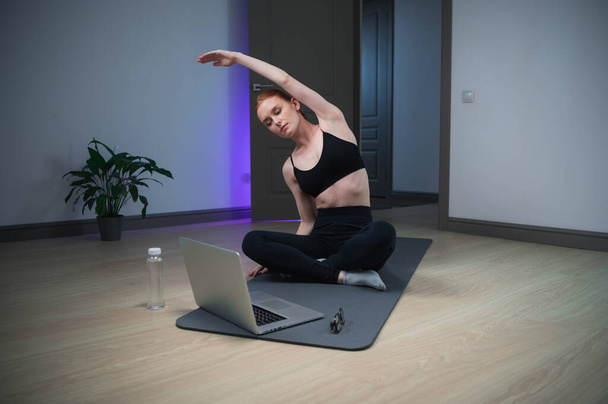 Kokenut joogavalmentaja suorittaa luokkansa kannettavan tietokoneen ja Internetin avulla, tyttö näyttää, miten vetää kunnolla käsivarsien ja selän lihaksia. - Valokuva, kuva