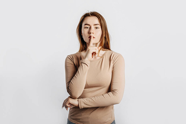 Shh gesture. Young beautiful serious brunette girl holding a finger to her lips on a white isolated background - Фото, зображення