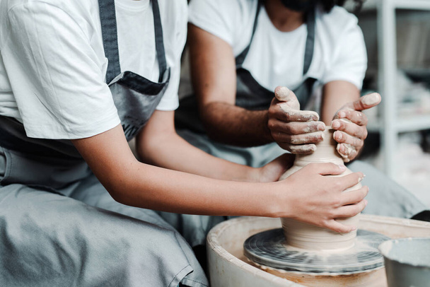 A girl and a man in aprons in a clay workshop. Male and female hands make clay vases - Fotoğraf, Görsel