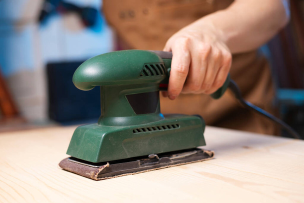 Closeup de carpinteiro lixar tábuas de madeira com máquina de lixar elétrica. Um carpinteiro retifica madeira com máquina de lixar. - Foto, Imagem