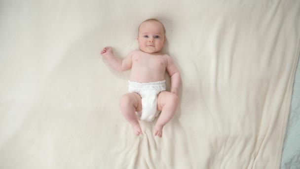 Bebek bezi takmış, yumuşak beyaz battaniyeye uzanmış küçük bir çocuğun manzarası. - Video, Çekim
