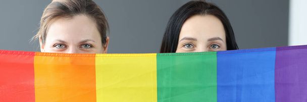 Dwie kobiety trzymają flagę lgbt przed sobą. - Zdjęcie, obraz