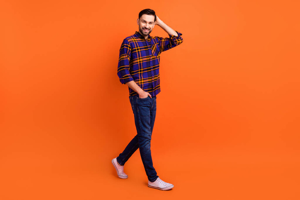 Full body profile photo of satisfied young man arm on head beaming smile isolated on orange color background - Фото, зображення
