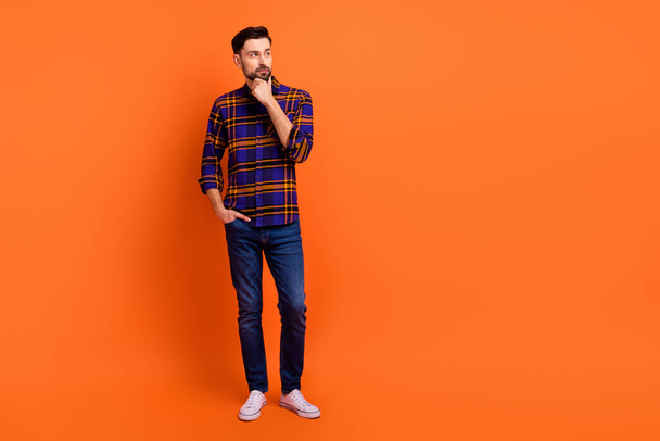 Full length photo of handsome guy arm on chin look interested empty space isolated on orange color background - Фото, зображення