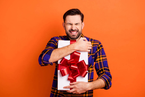 Photo of cheerful person closed eyes toothy smile hands hold hug giftbox isolated on orange color background - Photo, image