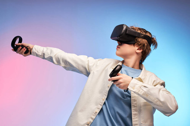 portrait of young guy in VR helmet holding device in hands on colourful background - Foto, afbeelding