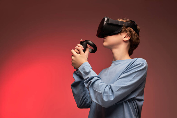 Amazed young teen boy wearing virtual reality vr headset gesturing hands - Foto, imagen