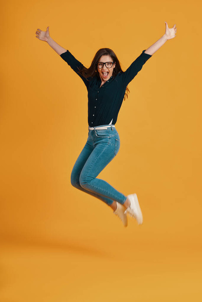 Full of length beautiful young women screaming and jumping against yellow background - Foto, imagen