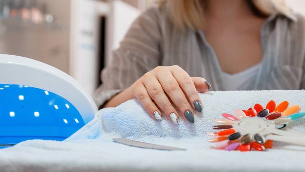 Woman with artificial acrylic nails picks up new polish color during manicure procedure. Manicure process in beauty salon. Hygiene beauty of hands in nail salon. Long web banner - Fotoğraf, Görsel
