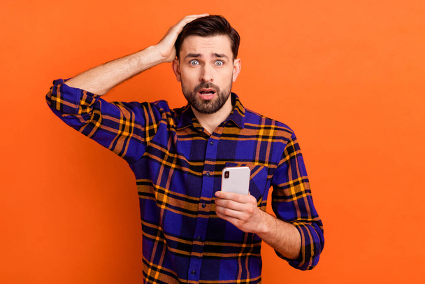 Photo of young man unhappy upset hand touch head use cellphone worried mistake fail problem isolated over orange color background - Foto, immagini