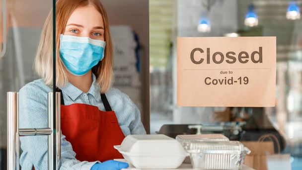 Woman waiter in protective medical mask gloves work with takeaway orders. Waiter giving takeout meal while lockdown shutdown. Food delivery against sign closed due to covid 19. Long web banner - Foto, imagen