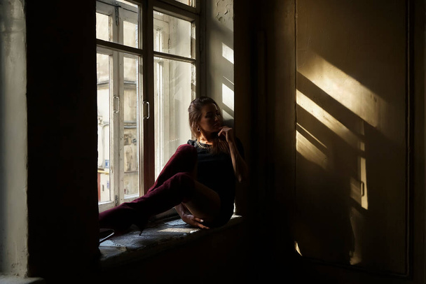 A dreaming woman with a long hair sits on the window sill. - Фото, изображение