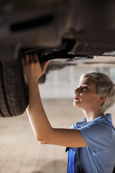 Professional female mechanic holding tools fixing undercarriage of vehicle, tire - 写真・画像