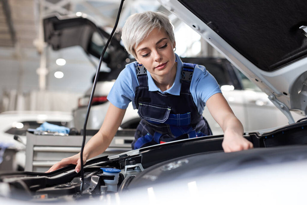 Short haired female professional master repairing car in workshop at workplace - 写真・画像