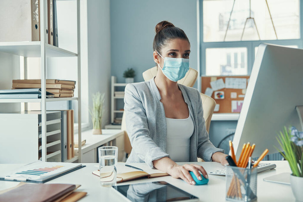 Beautiful young woman in smart casual wear and protective mask using computer - Fotografie, Obrázek