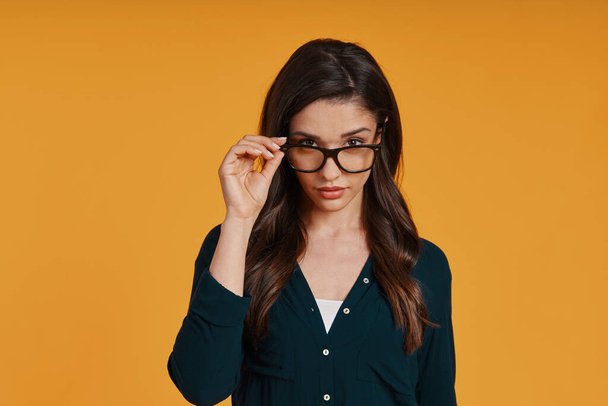 Beautiful young woman in casual clothing adjusting eyewear and looking at camera - Фото, изображение