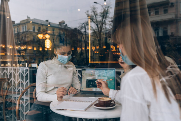 Las amigas se conocieron en un café. Usar máscaras protectoras médicas. - Foto, imagen