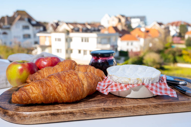 Γαλλικό πρωινό με φρέσκα ψημένα κρουασάν και τυριά από τη Νορμανδία, καμαμπέρ και neufchatel σερβίρεται εξωτερική με ωραία θέα γαλλικό χωριό - Φωτογραφία, εικόνα