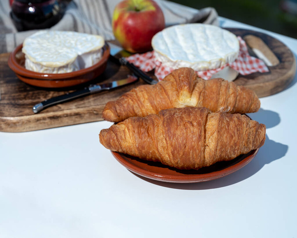Desayuno francés con cruasanes recién horneados y quesos de Normandía, camembert y neufchatel servido al aire libre con bonitas vistas al pueblo francés - Foto, Imagen