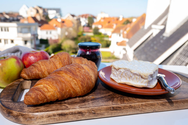 Französisches Frühstück mit frisch gebackenen Croissants und Käse aus der Normandie, Camembert und Neufchatel serviert im Freien mit schönem Blick auf das französische Dorf - Foto, Bild